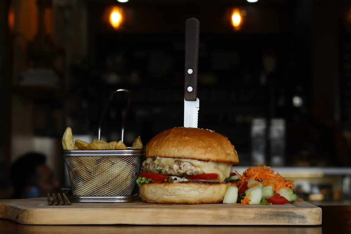 A house burger with melted cheese, fries and a side salad on a wooden board