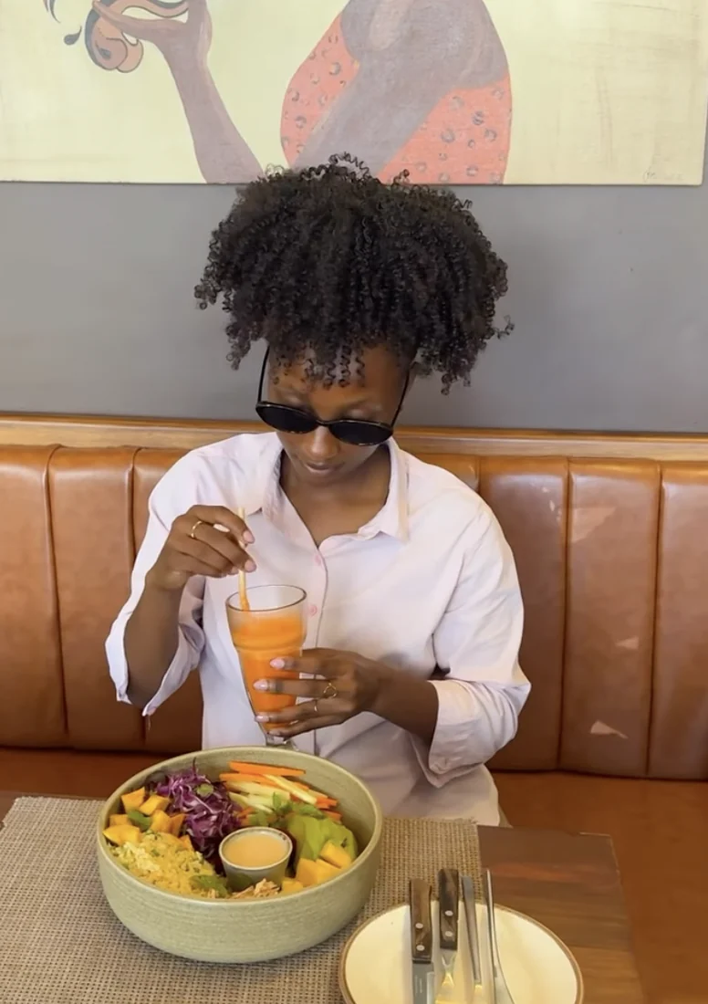 A guest with a fresh juice and a Buddha bowl in a booth beneath the wall art