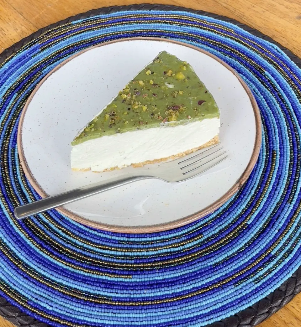 A slice of pistachio cheesecake on a beaded table setting